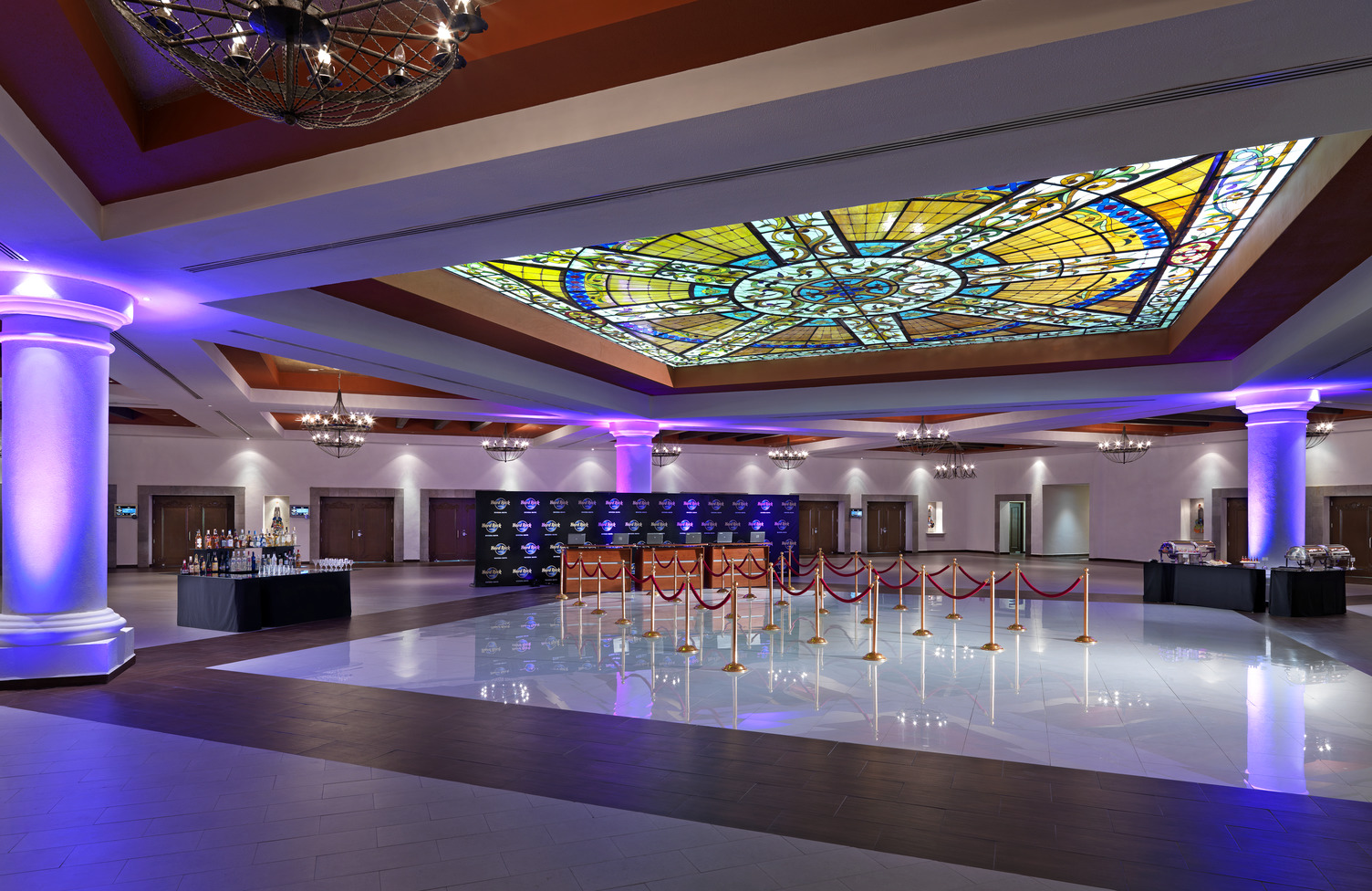 Spacious foyer with stained glass ceiling, ornate columns, arranged cocktail tables, and a barricade for events.