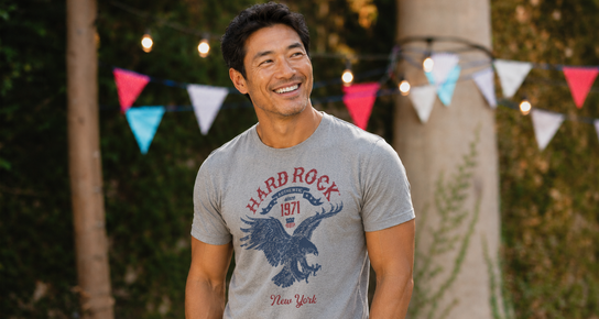 Man wearing a gray Hard Rock New York graphic T-shirt at an outdoor summer cookout.